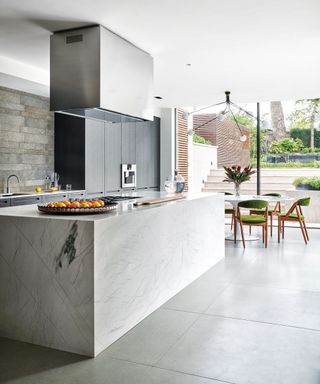 Kitchen with grey tiled concrete floor, large marbled kitchen island, floor to ceiling glass doors to the patio and garden. Hammered basalt feature wall.
