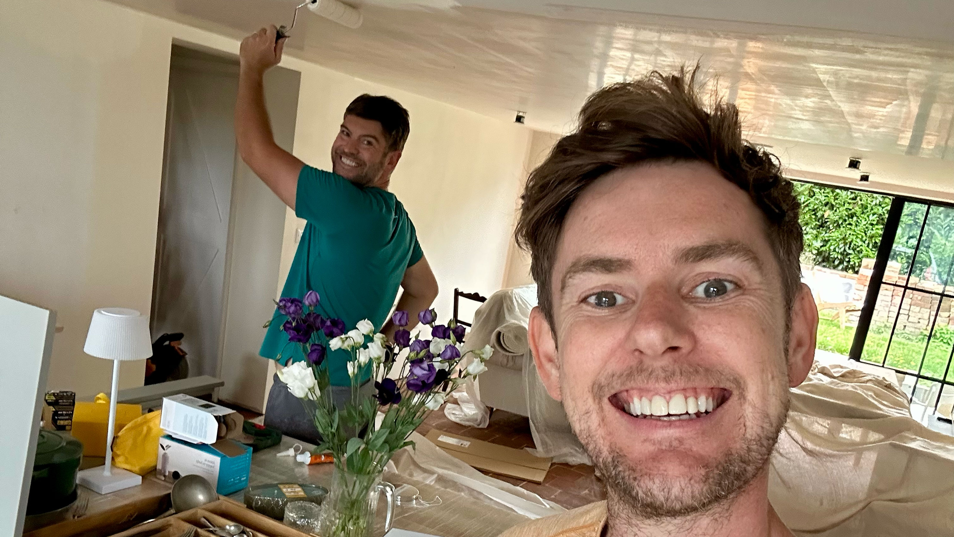 Two men in kitchen, one taking selfie, one painting the ceiling