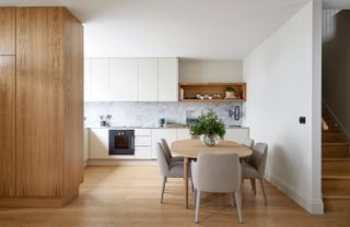 Kitchen with white cupboards, square table, chairs and wooden floors.