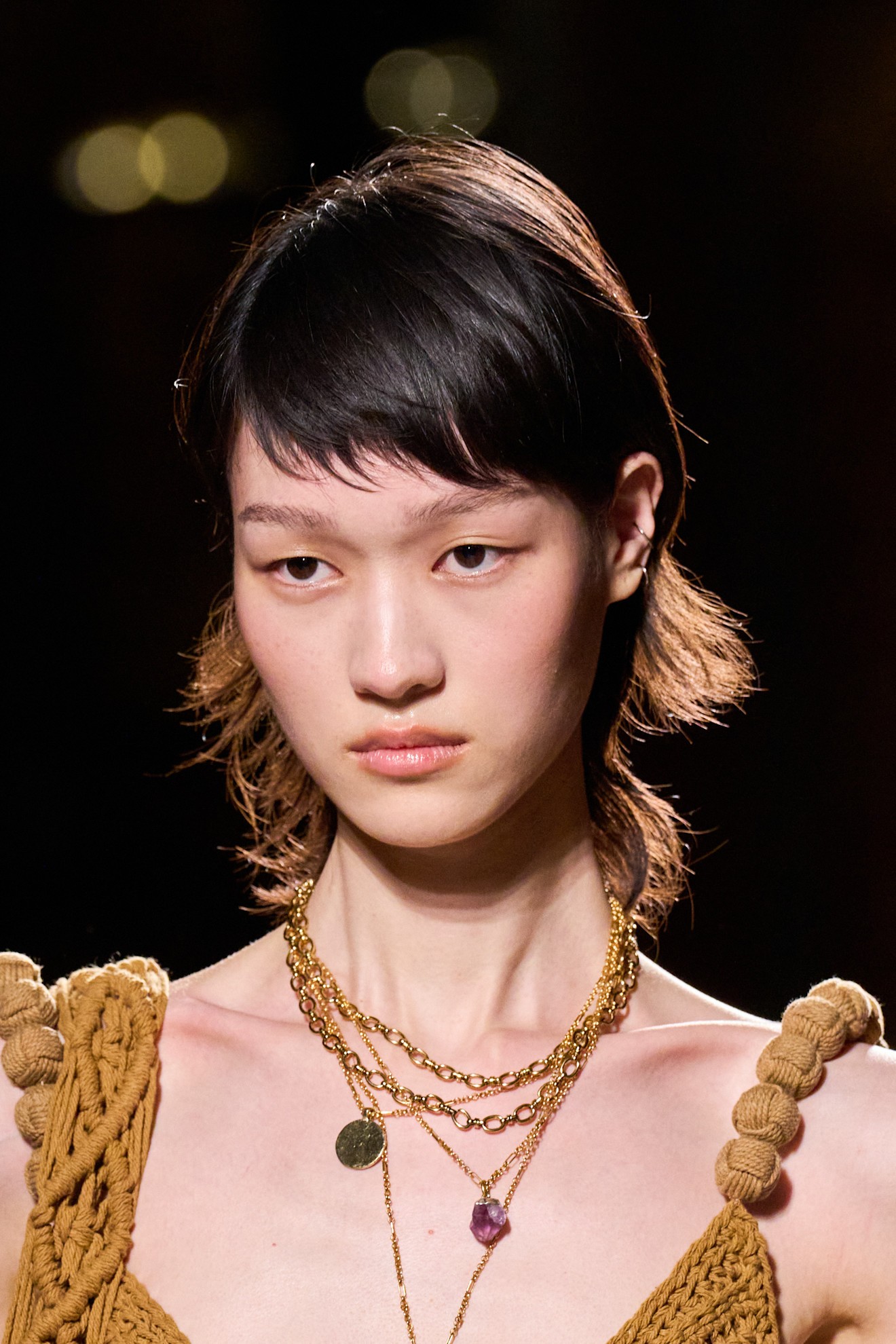 A model with a modern crop haircut in a mustard yellow knit top