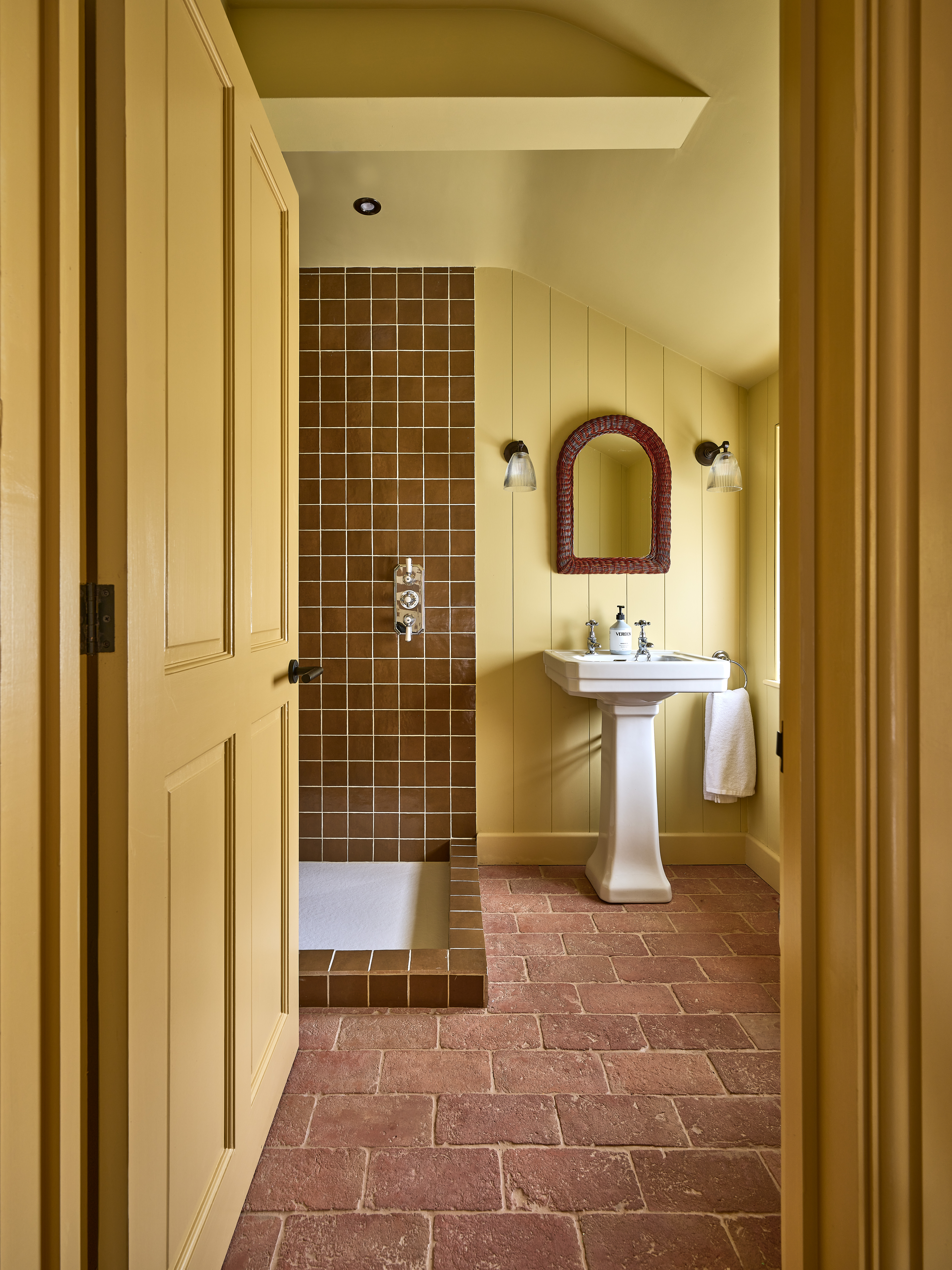 yellow painted bathroom, including the door and door frame, with brick floors and brown tiled shower