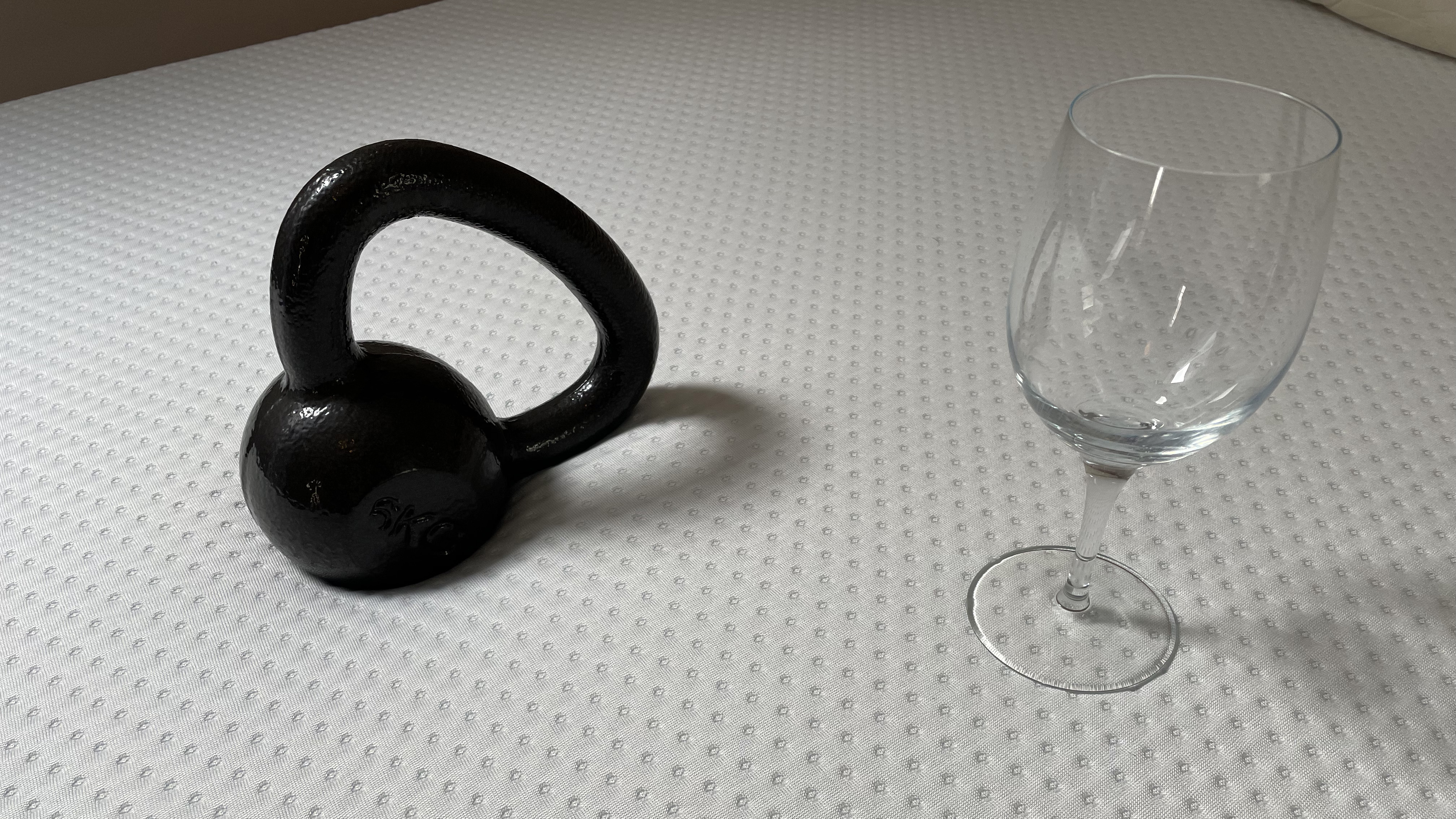 Image shows a 6KG weight dropped next to a wine glass placed on the Emma Mattress during a motion isolation test