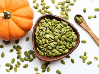 An overhead view of pumpkin seeds in a bowl next to a small pumpkin