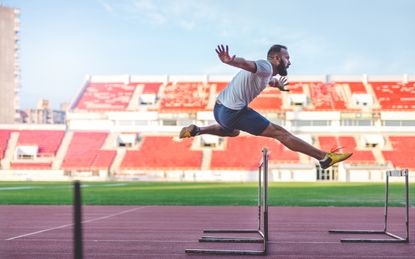 35 years old man at the stadium. He is jumping over the hurdle, and improving his jumping skills