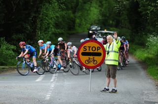 Volunteer stops traffic with a sign at a bike race on a British road