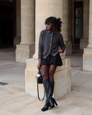 French woman wearing cardigan, black miniskirt, and tall black boots