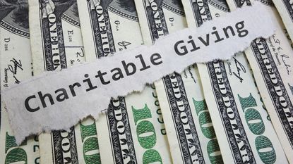 The words "charitable giving" on a torn piece of paper atop spread-out hundred-dollar bills.