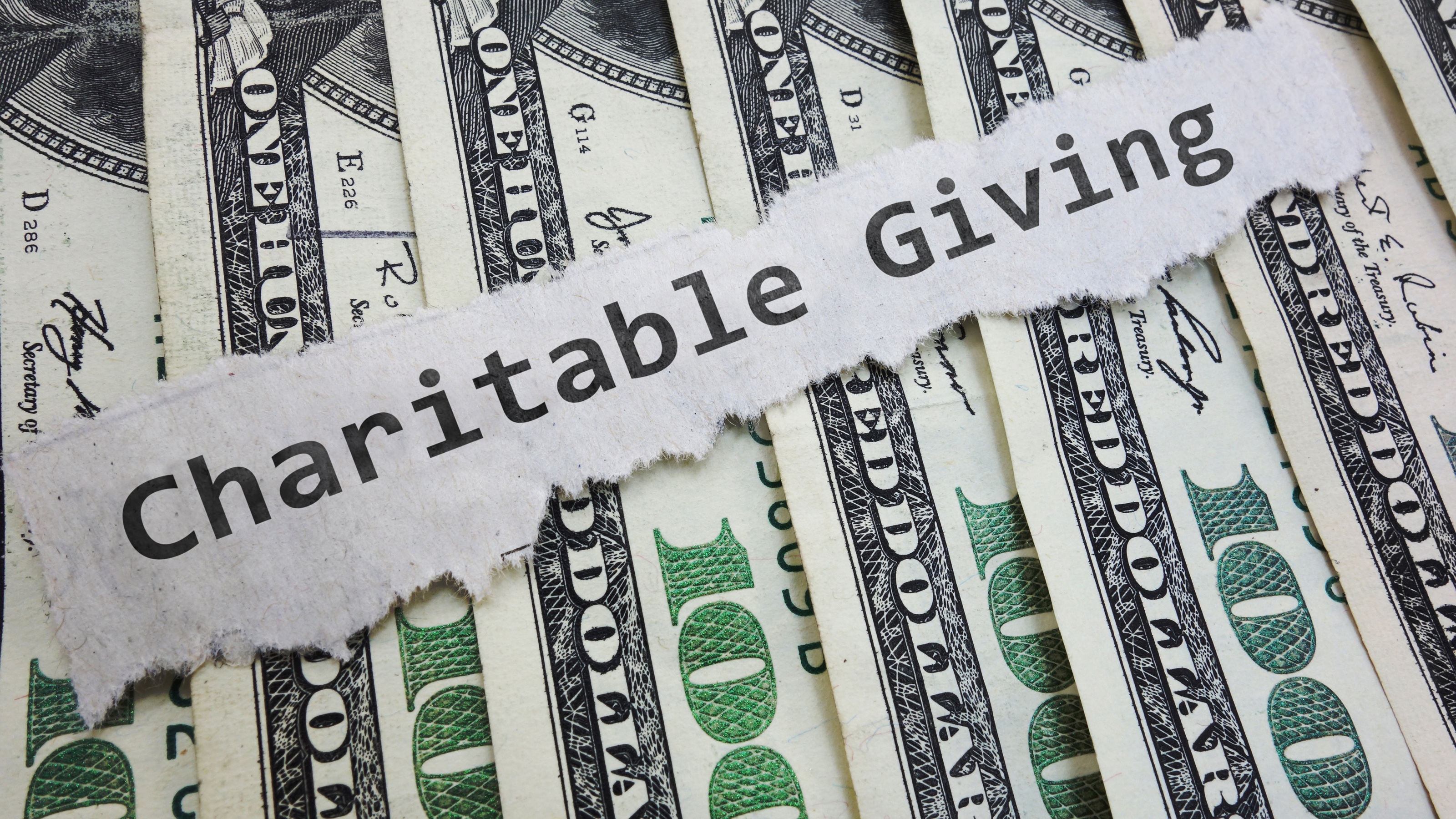 The words "charitable giving" on a torn piece of paper atop spread-out hundred-dollar bills.