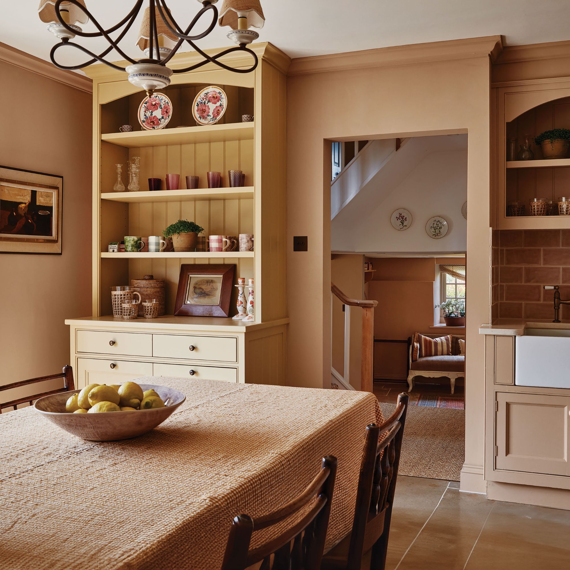 Kitchen diner with dusty pink walls and cabinetry, wooden chairs and pink tablecloths, yellow cabinet