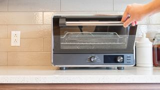 A toaster oven in a kitchen with a hand pulling the door down