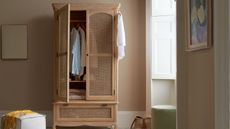 The Margot free standing wardrobe with a partially open door full of lcothes, beside a small white square pouffe stool