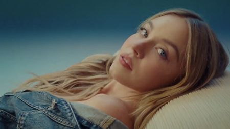 For a controversial American Eagle ad, Sydney Sweeney reclines, stares into the camera, and wears a denim jacket off the shoulder.