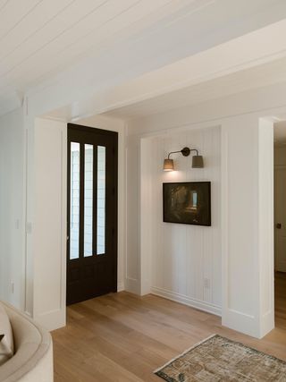 A light entryway with dark wood door and sconces on the light wall and a patterned rug.