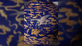 The image shows an 18th-century Chinese blue vase decorated with silver cranes and gold bats and clouds. This is a close up on the silver crane.
