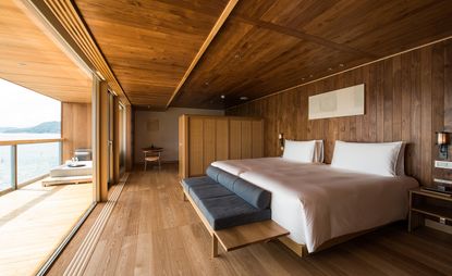 hotel guest bedroom with wooden floors, walls and ceiling, sliding doors with view out to water