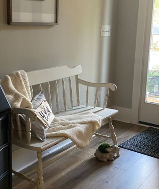 White wooden entryway bench with white blanket over the top, in foyer with wooden flooring