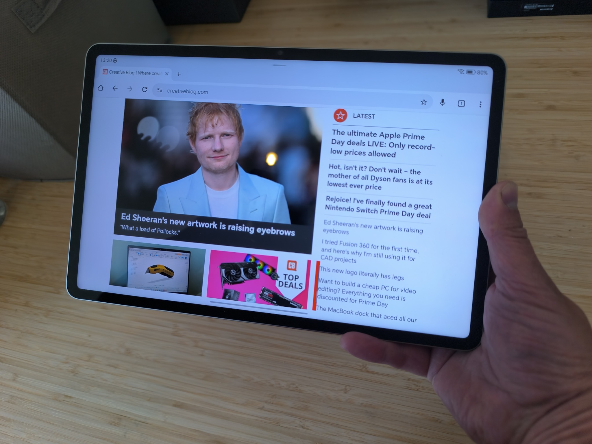 Hand holding tablet showing homepage of Creative Bloq featuring Ed Sheeran