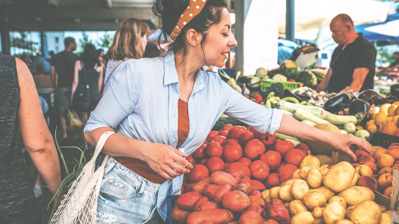 Woman picking fresh, seasonal fruit at a market, a money-saving health trick