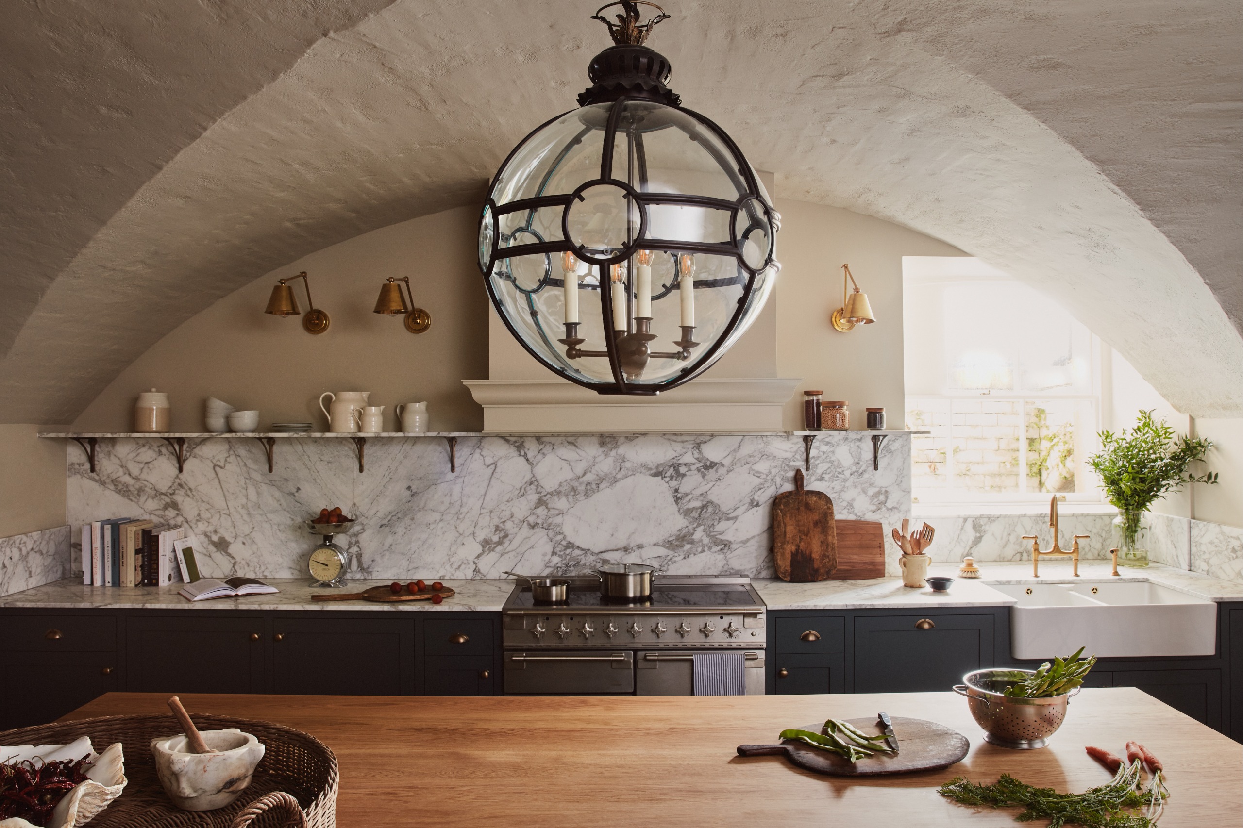 A vaulted country-house kitchen with. blue cabinets, marble countertops, a circular glass ceiling top and wooden butcher's block