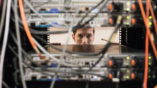 Man working in computer roomm peeking between servers, ethernet cable in hand - stock photo