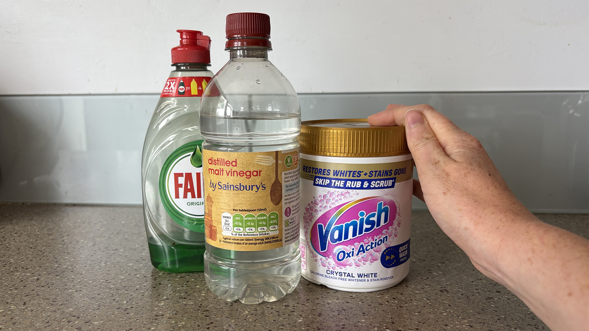 A closeup of dish soap, white vinegar and oxygen bleach in the kitchen, with our tester's hand in shot