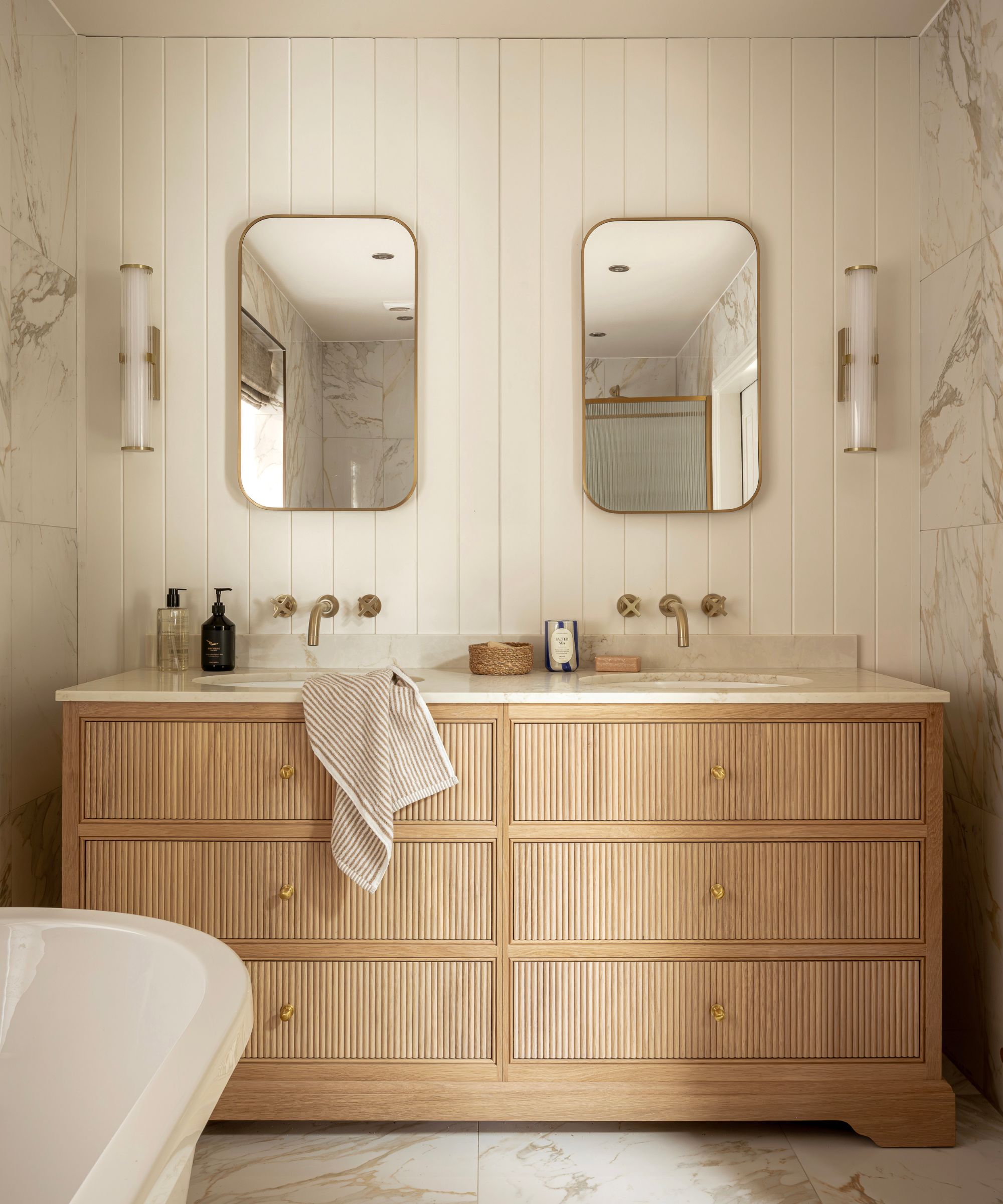 A neutral bathroom with a wooden vanity, paneled walls, and gold hardware