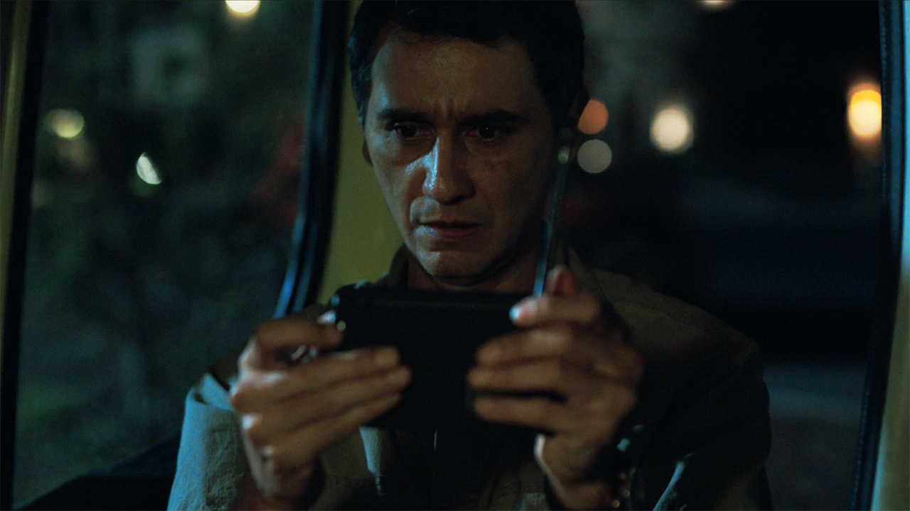 Manousos looking at a portable radio at night in Pluribus episode 9