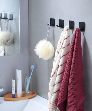 An image of black peel and stick wall hooks in a bathroom with towels hanging off them, with a toothbrush and toothpaste in the background