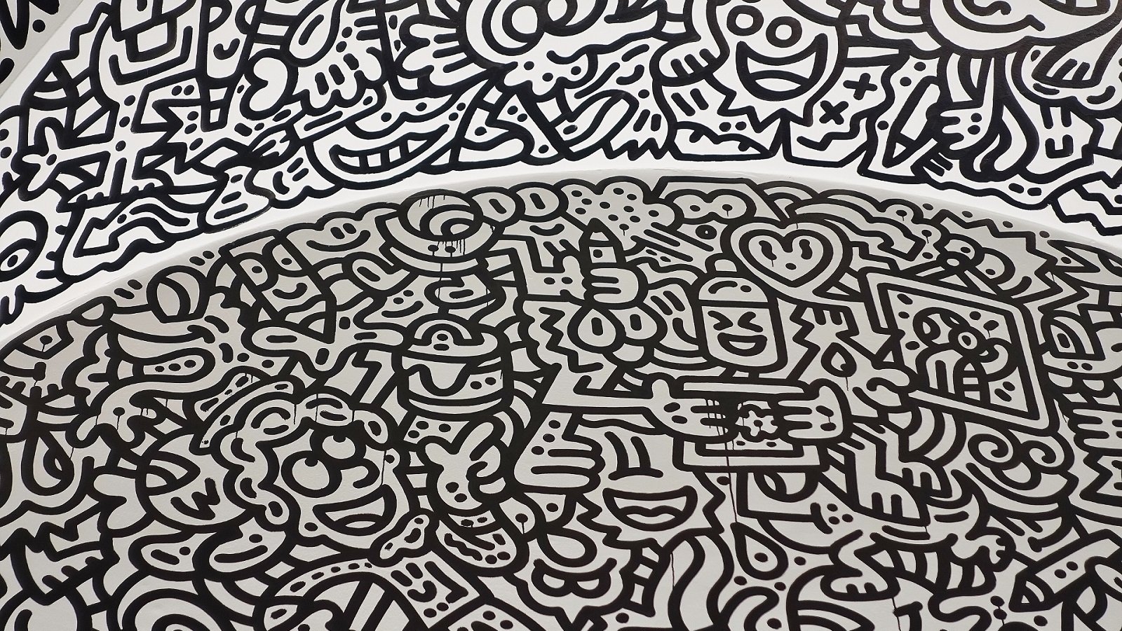 Mr Doodle drawings on part of the ceiling dome in an art gallery, using black paint on a white wall. The doodles are large and thick with motifs like robots, squiggles and hearts. Paint drips in some sections.