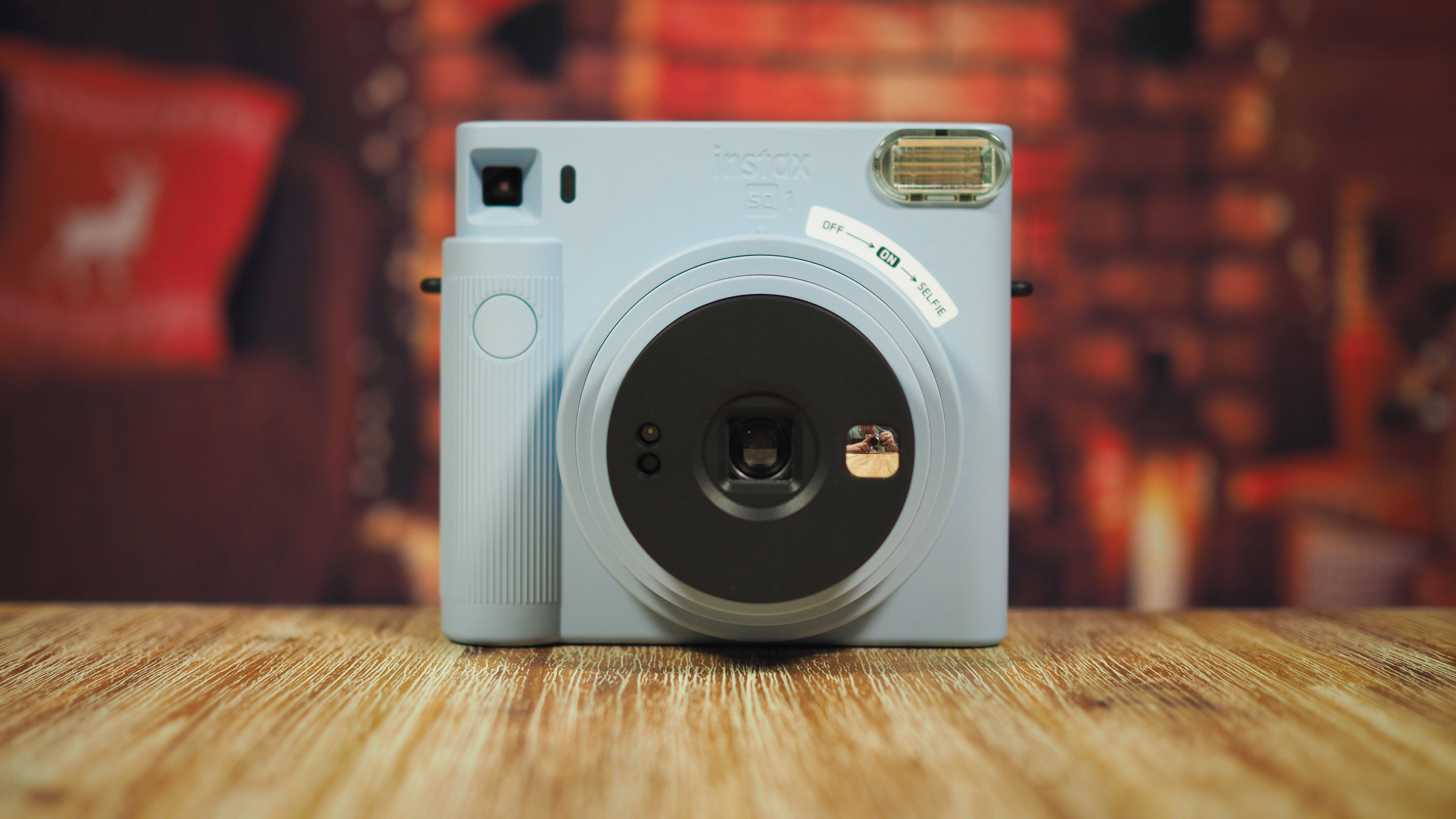 Light blue instant film camera placed on a wooden surface with a blurred warm-toned background
