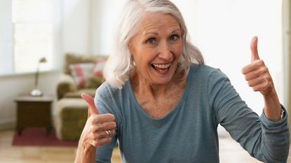 A smiling gray-haired woman gives two thumbs up.