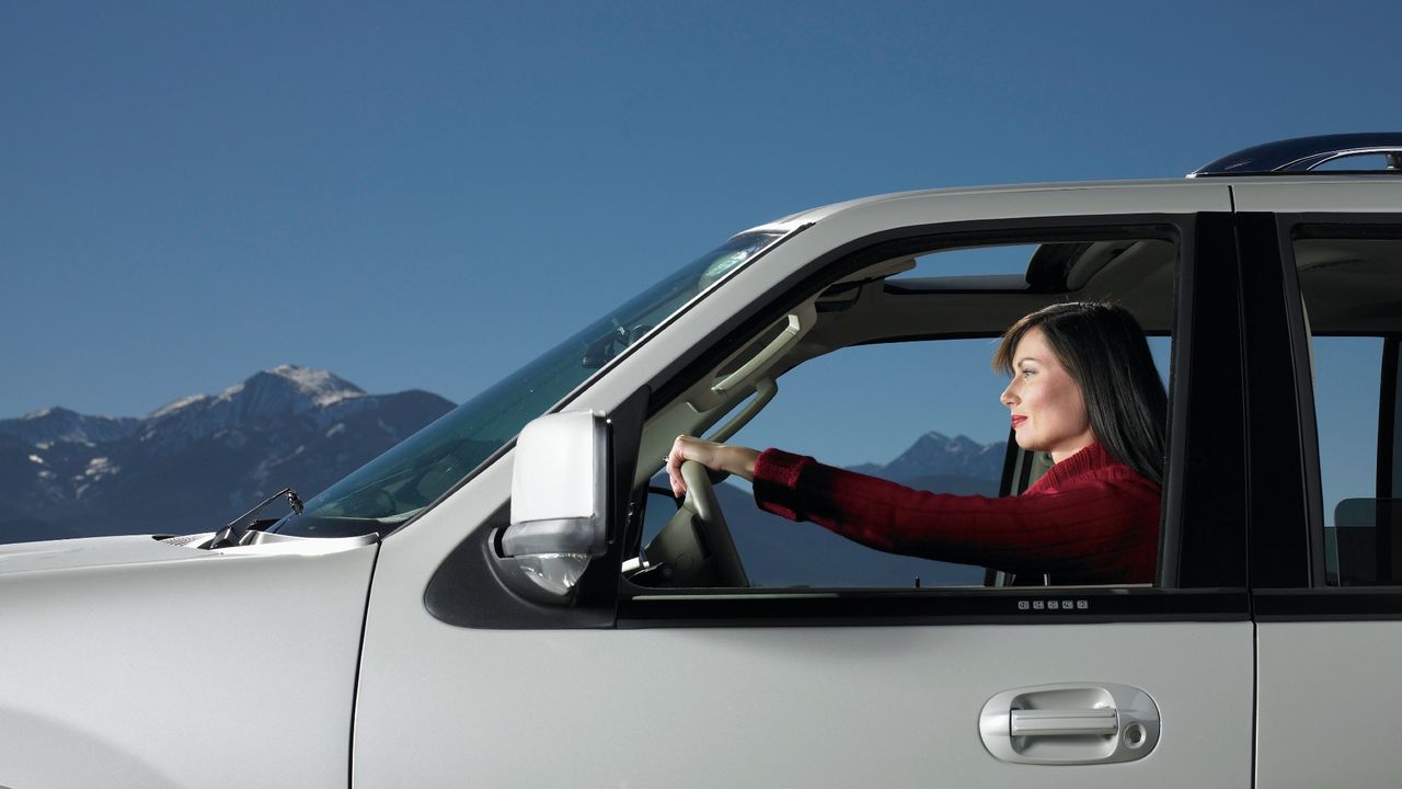 Side view of a woman driving a big SUV with a blue sky and a mountain in the background