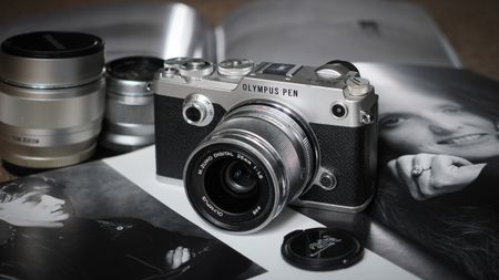 Olympus PEN-F (2016) sitting on a photography book, surrounded by lenses and a lens cap