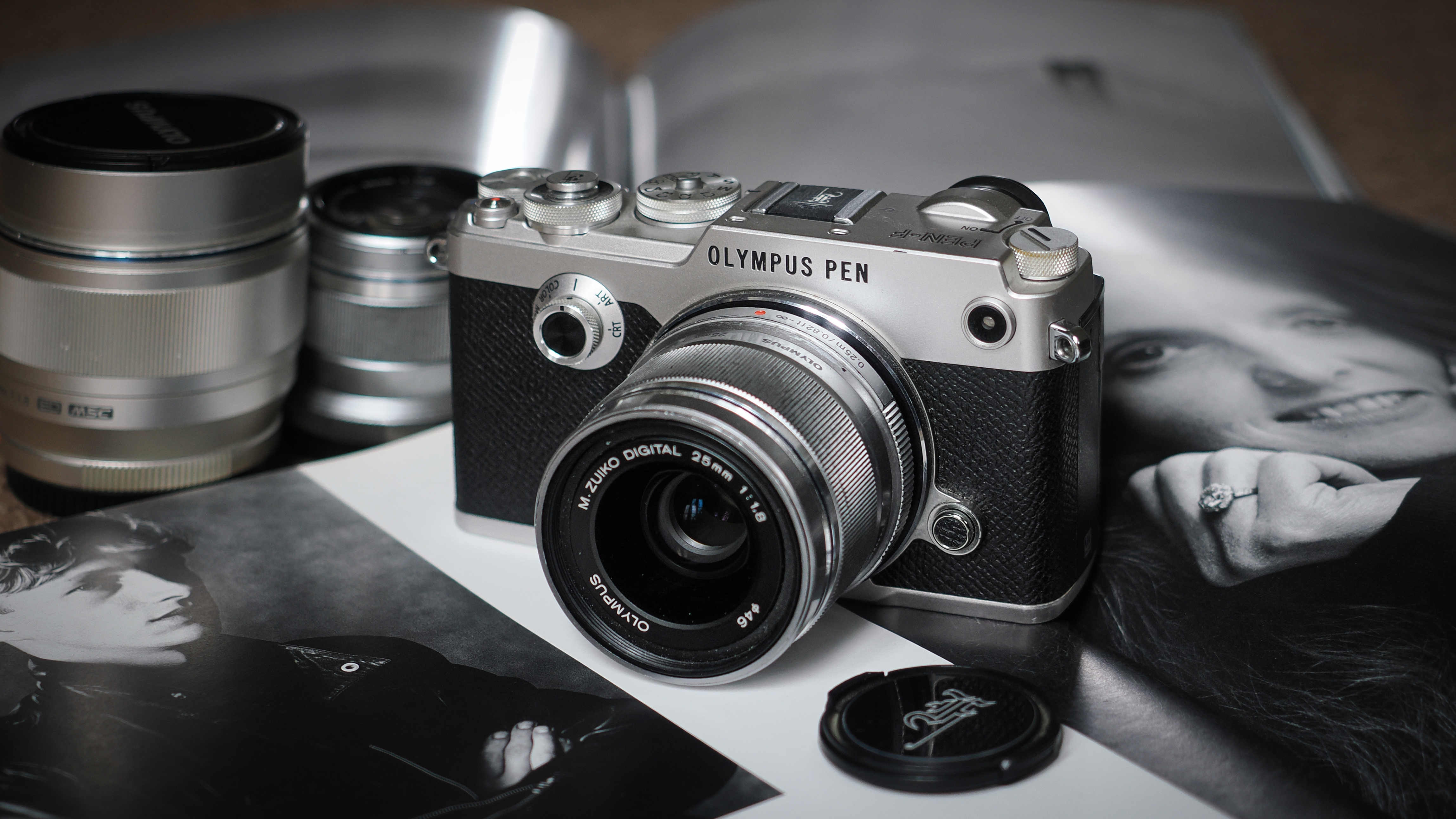 Olympus PEN-F (2016) sitting on a photography book, surrounded by lenses and a lens cap