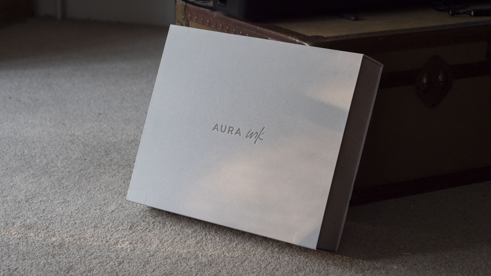 The Aura Ink 'E Ink' digital photo frame's presentation box, propped against a chest, illuminated by the golden hour sun