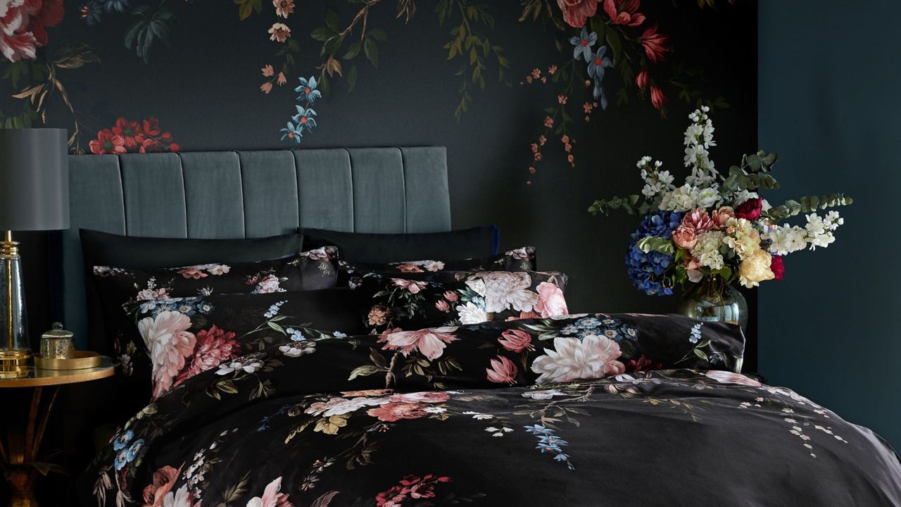 Dark bedroom ideas are so dreamy. Here is a black bedroom with floral wallpaper, a gray bed with black floral bedding, and a wooden floor