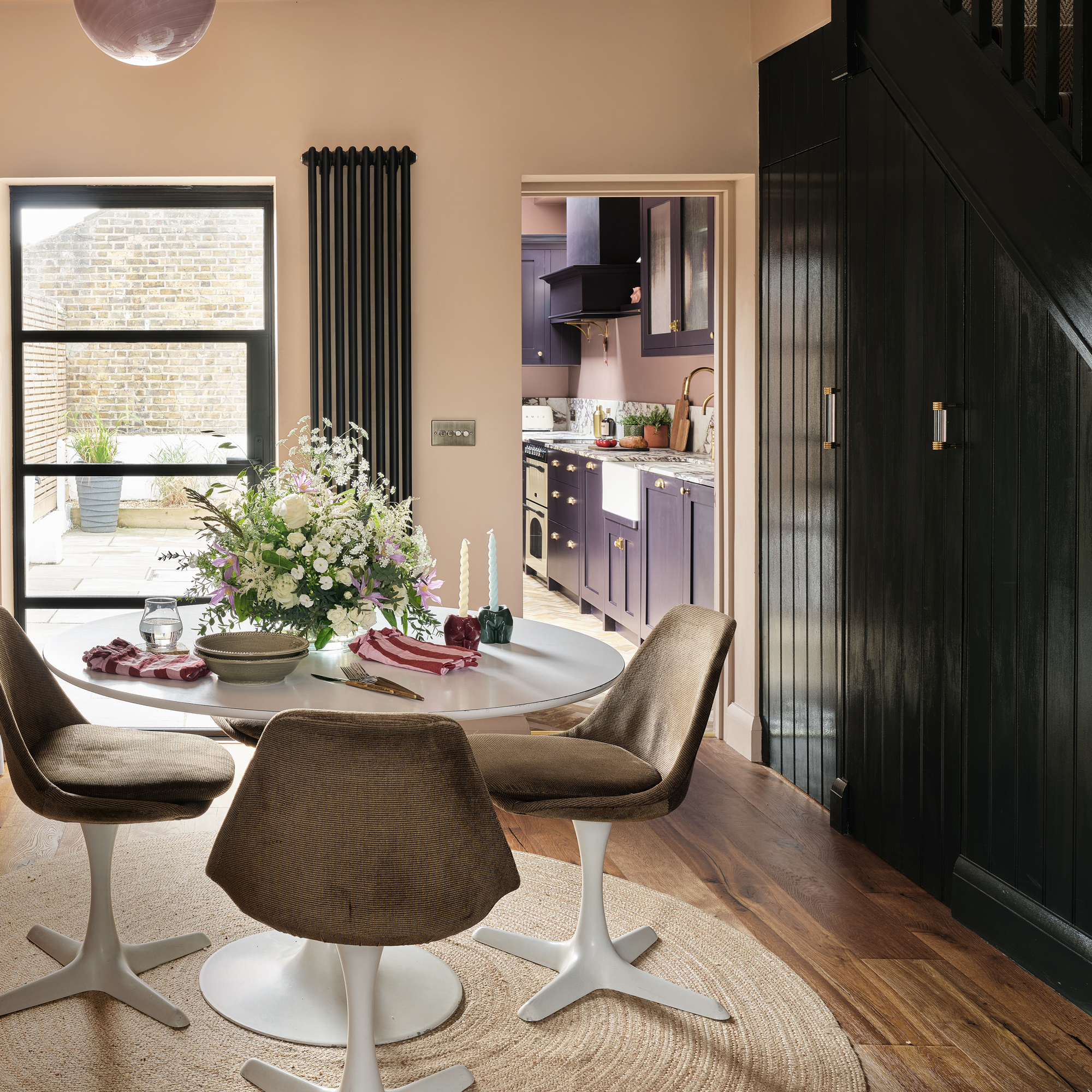 an open plan dining room with a Tulip table and matching upholstered chairs, fitted storage and a view into the kitchen and garden