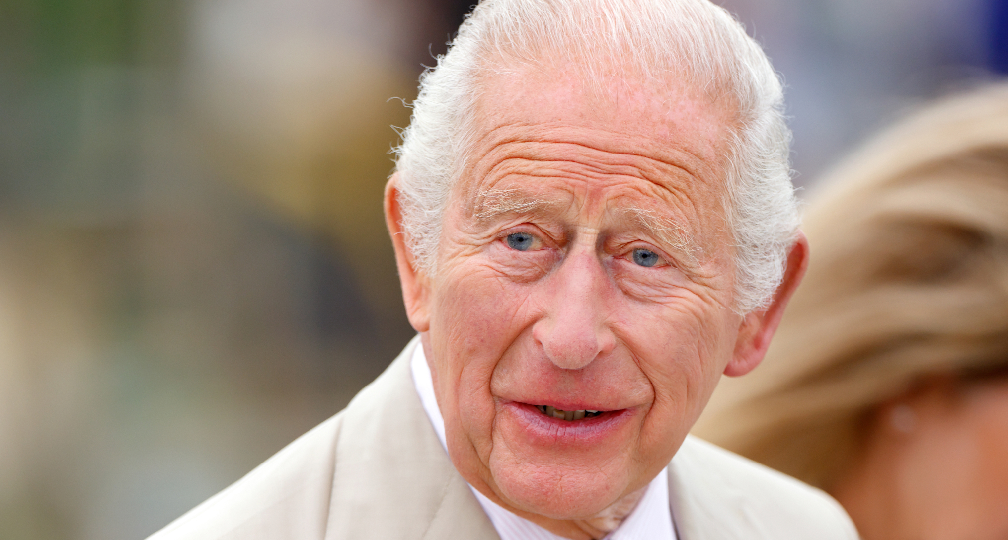 King Charles wearing a tan suit and smiling