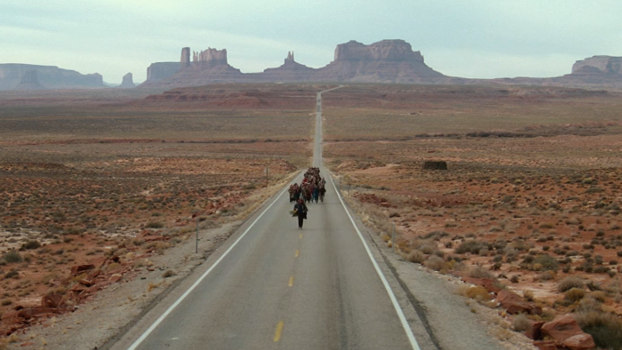 A group of runners running down a long highway in the desert