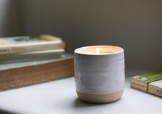 A lit candle in a ceramic jar on a desk surrounded by books