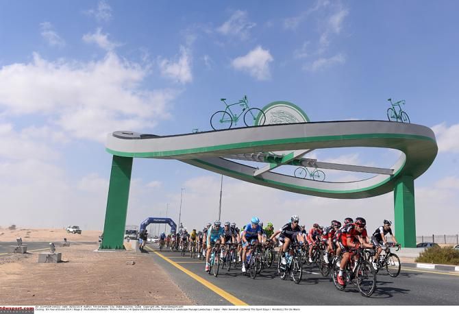 Riders pass under a cycling sculpture
