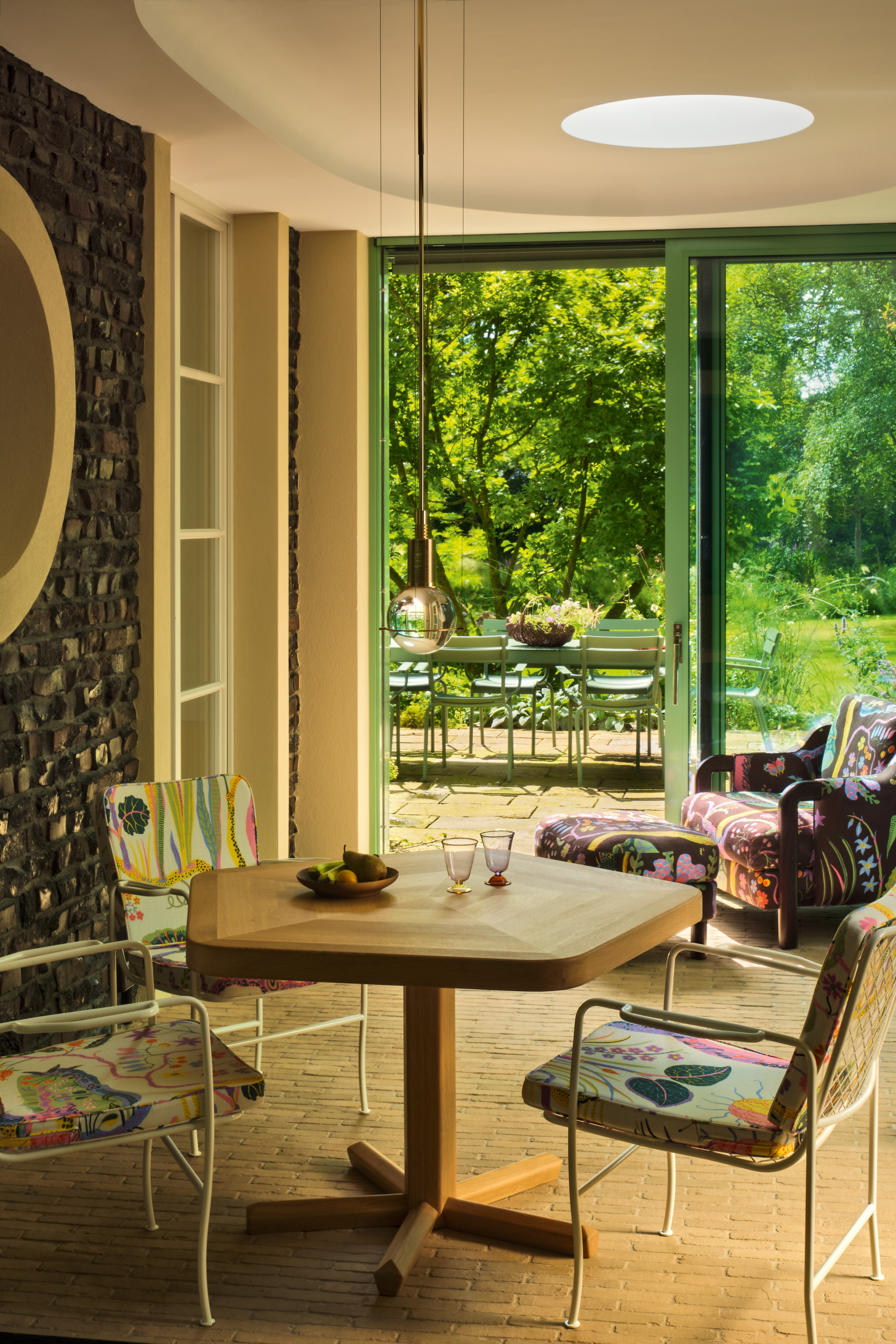 View from garden room with brick floor and green glazed doors with pentagonal table and botanical patterned chairs