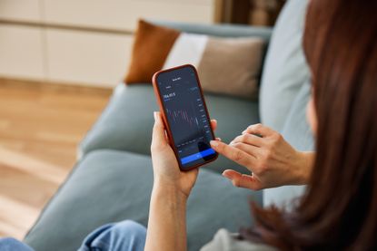 woman at home uses a smartphone trading app to monitor stocks funds and investment trusts