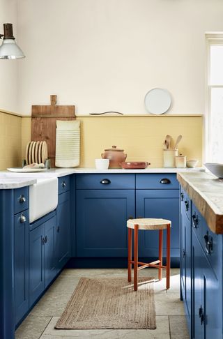 A small galley kitchen with blue cabinetry, pale yellow walls and stone flooring