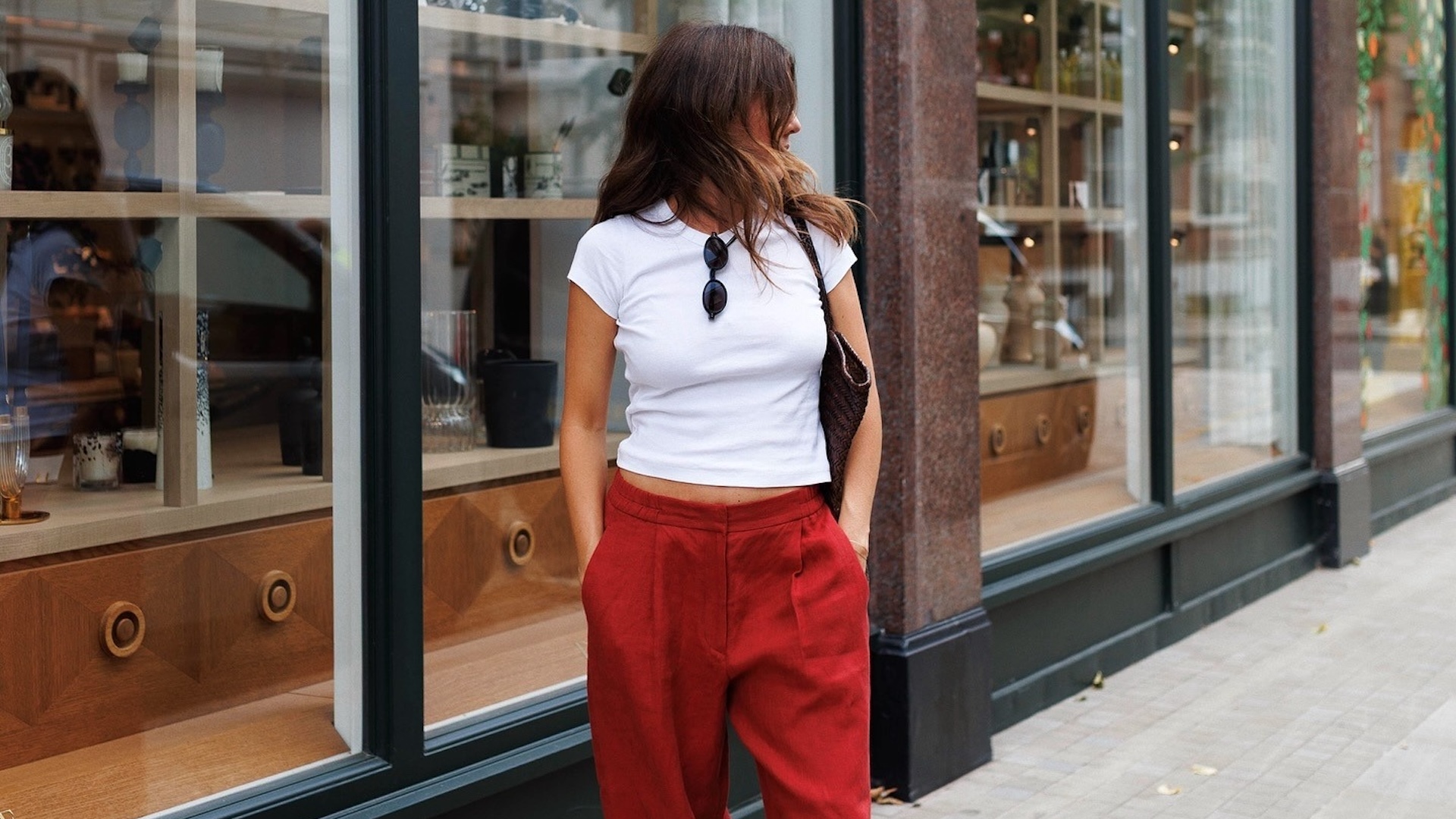 British style influencer Kim Turkington poses on a London sidewalk wearing a white T-shirt, brown woven bag and red linen pants