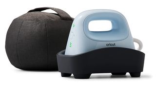 The best Cricut machines; a small grey iron-shaped device sat in a black holder, it has a small hole for a person's hand and three green lights