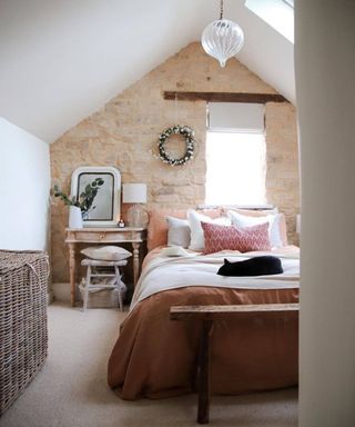 bedroom in loft with cream carpet exposed stone wall, double bed and vintage wooden furniture