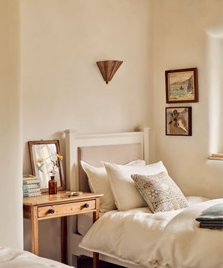 Neutral single bedroom with white wooden bed and antique nightstands with summery wall decor