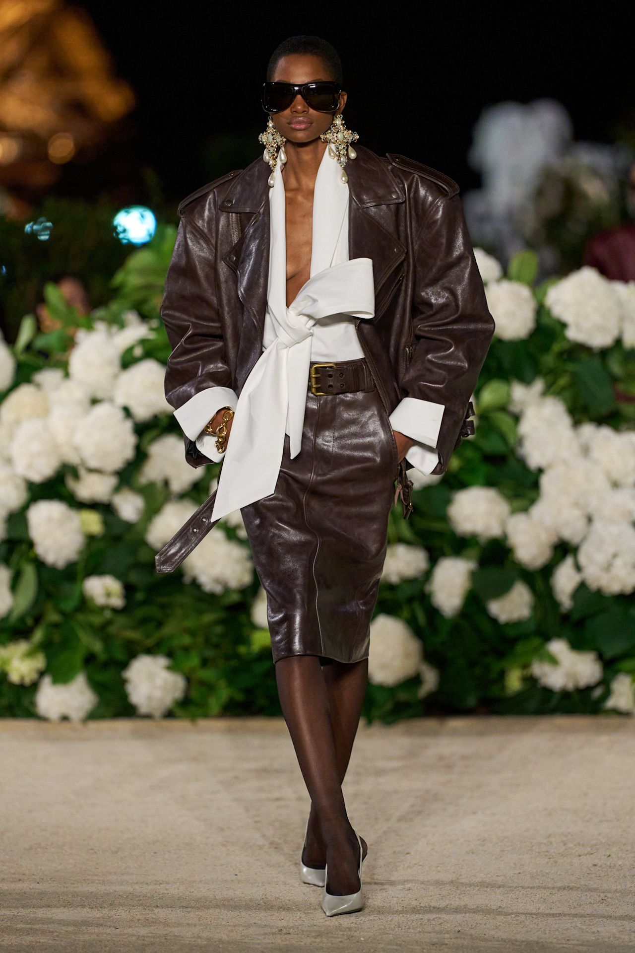 A model at Saint Laurent Spring 2026 wearing a white bow blouse, brown leather jacket, and brown leather pencil skirt