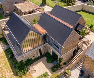 exterior shot of large three section eco house with black pitched roofs, solar panels, timber cladding, stone walls set in large courtyard and garden area